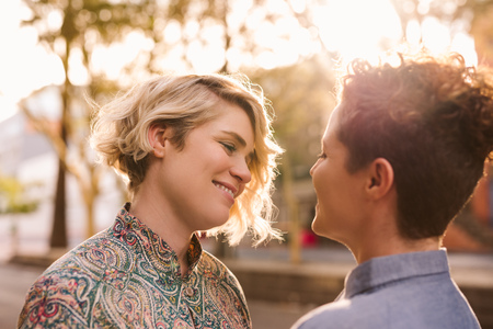 Smiling lesbian couple standing outside looking into each others eyesの写真素材