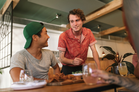 Young waiter talking with a group of smiling bistro customers