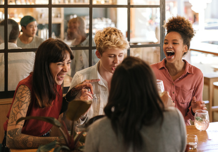 Diverse group of girlfriends laughing together in a trendy barの写真素材