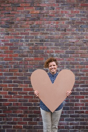 Smiling young woman holding a large heart while standing outsideの写真素材