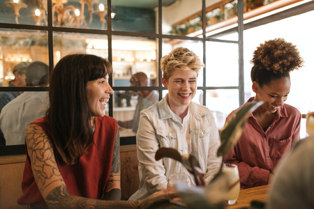 Smiling young female friends talking together in a trendy bistroの写真素材