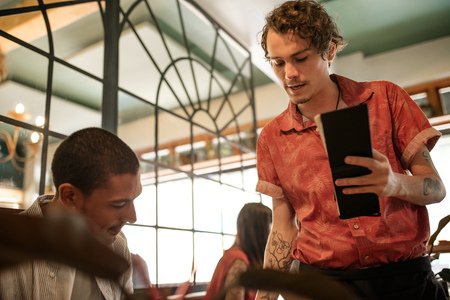 Waiter explaining the menu to a smiling restaurant customerの写真素材