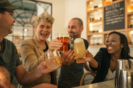 Friends hanging out together in a bar cheering with drinks