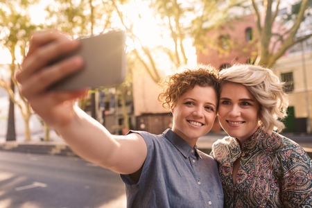 Smiling lesbian couple taking a selfie together in the cityの写真素材