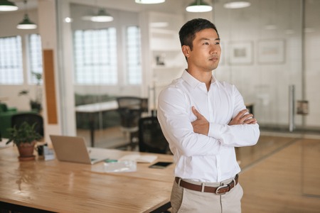 Focused Asian businessman standing in an office deep in thoughtの写真素材