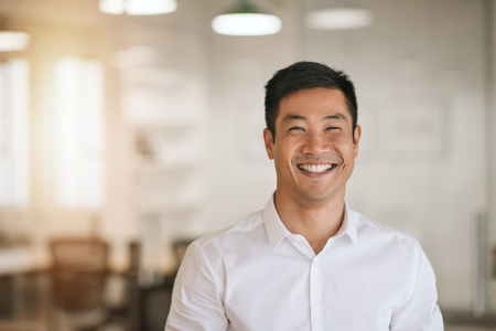 Smiling Asian businessman standing in a bright modern officeの写真素材