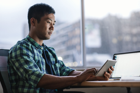 Young Asian designer using a tablet at his office workstationの写真素材