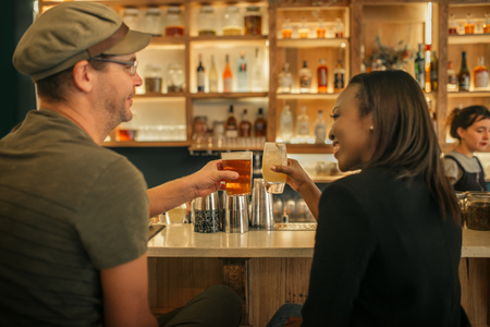 Two smiling friends sitting in a bar cheering with drinksの写真素材