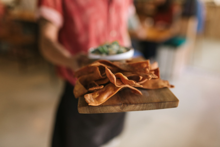 Closeup of a waiter standing in a trendy bistro holding a serving board with freshly made nachosの写真素材