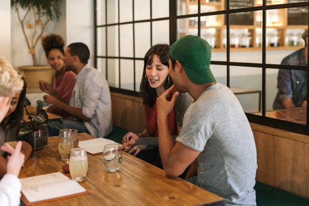 Smiling friends sitting and talking together at a bistro tableの写真素材