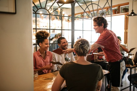 Group of smiling friends ordering food from a bistro waiterの写真素材