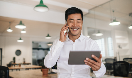 Smiling Asian businessman using a cellphone and tablet at workの写真素材