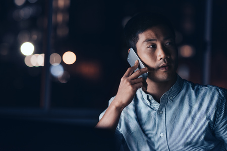 Young Asian businessman talking on his cellphone while working lの写真素材