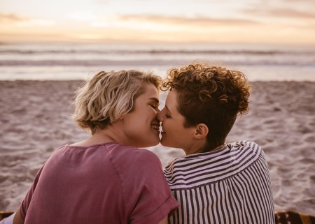 Romantic young lesbian couple kissing during a beach sunsetの写真素材