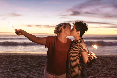 Romantic lesbian couple kissing and holding sparklers at the beachの写真素材