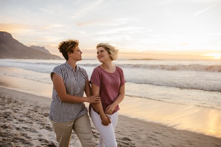 Smiling lesbian couple enjoying a romantic walk along a beachの写真素材