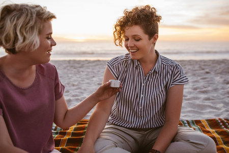 Young lesbian couple sitting on a beach blanket at duskの写真素材