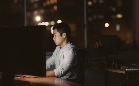 Young Asian businessman sitting at his workstation late at nightの写真素材