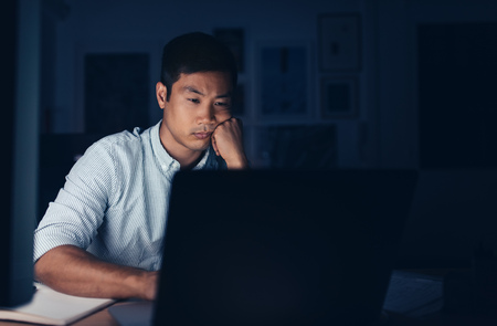 Tired Asian businessman working on a laptop late at nightの写真素材