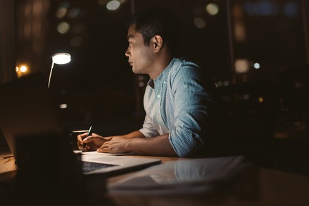 Young Asian businessman working online in a dark officeの写真素材