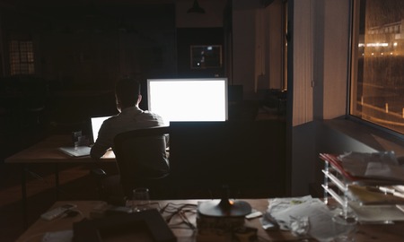 Businessman working online at his desk in a dark officeの写真素材