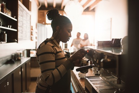 Young African barista frothing milk behind a cafe counterの写真素材