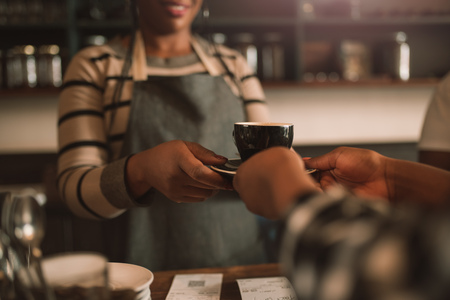 Smiling African barista giving her customer a fresh cappuccinoの写真素材
