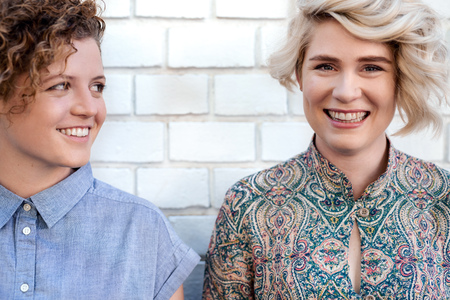 Young lesbian couple laughing while standing outside togetherの写真素材