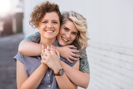 Smiling young lesbian couple standing affectionately together outdoorsの写真素材