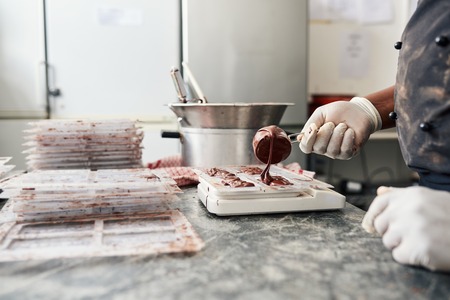 Worker pouring melted chocolate into molds to make bars