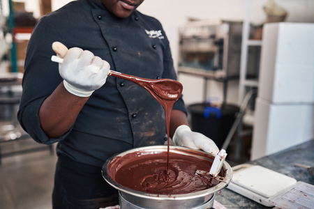 Worker holding a spoon full of artisanal melted chocolateの写真素材