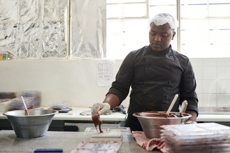 Worker putting melted chocolate into plastic molds to make barsの写真素材