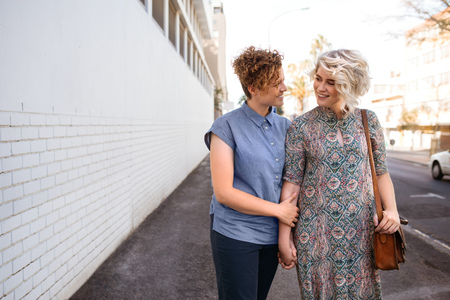 Smiling lesbian couple walking together in the city holding handsの写真素材