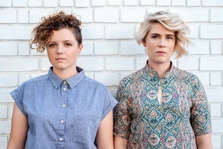 Young lesbian couple standing in front of a brick wallの写真素材
