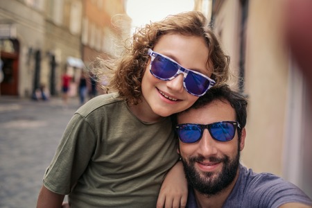 Smiling boy and his father taking selfies outside