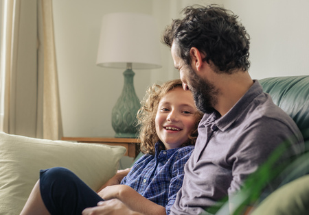 Boy and his father laughing together on their sofaの写真素材
