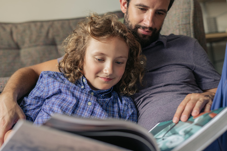 Father and son reading a book together at homeの写真素材