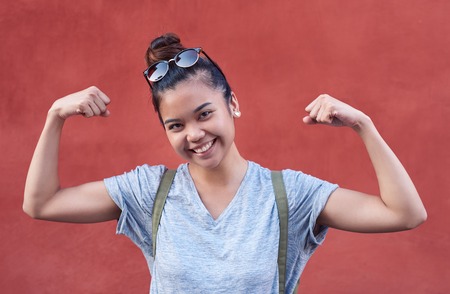 Smiling young Asian woman humorously flexing her arms outsideの写真素材