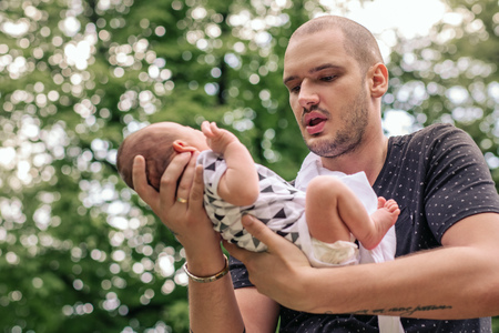 Young father cradling his baby boy in his hands outsideの写真素材