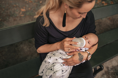 Mother sitting outside feeding her baby boy with a bottleの写真素材