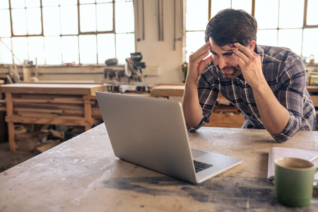 Stressed out woodworker using a laptop in his carpentry studioの写真素材