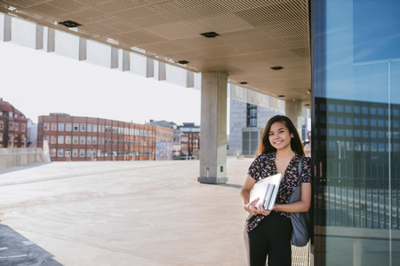 Smiling Asian university student standing on campus carrying textbooksの写真素材