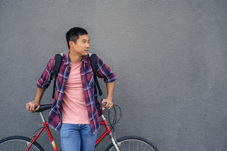 Young man leaning with his bike against a gray wallの写真素材