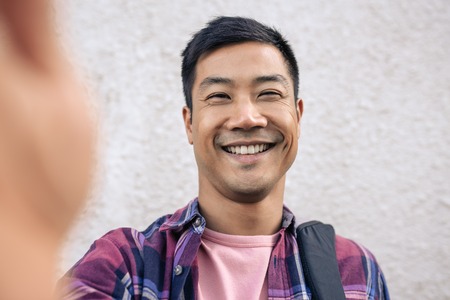 Smiling young Asian man taking a selfie in the cityの写真素材