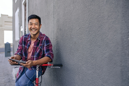 Smiling young man leaning on his bicycle using a tabletの写真素材