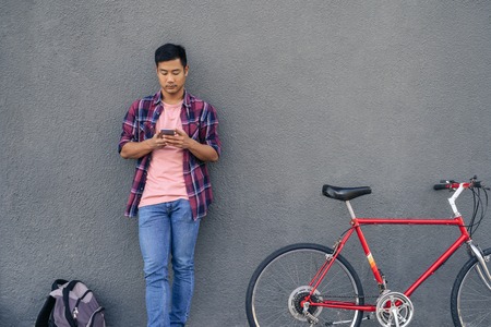 Young man sending a text while standing with his bikeの写真素材
