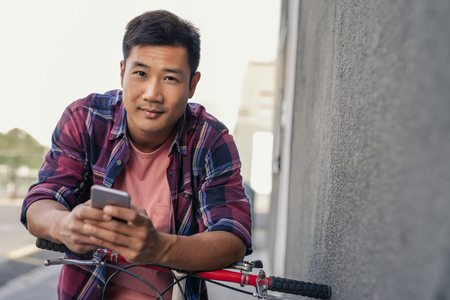 Smiling young man leaning over his bike reading a textの写真素材