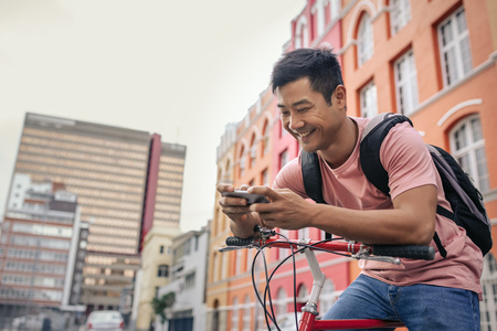 Smiling young man sitting on his bike sending a textの写真素材