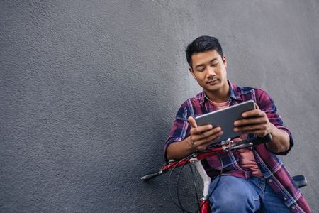 Young man leaning on his bicycle using a tabletの写真素材