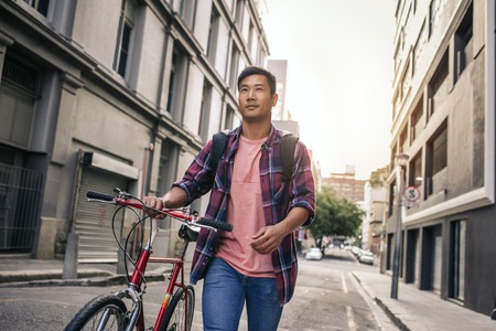 Young man walking with his bike down a city streetの写真素材